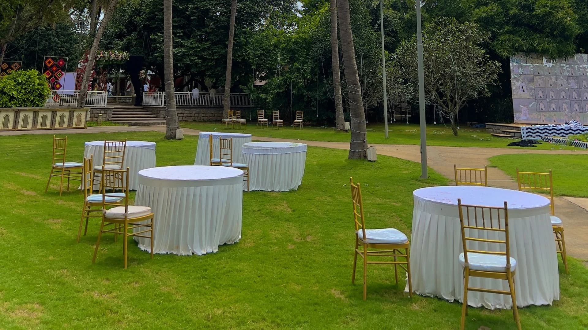 Outdoor event setup with round tables and gold chairs beneath palm trees